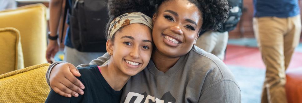 Two students smiling with their arms around each other