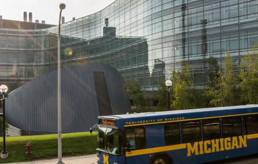 Maize and blue colored bus driving on campus