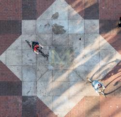 Two students biking across the block M on the Diag