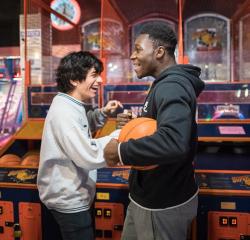 Two students shooting hoops at an arcade and laughing