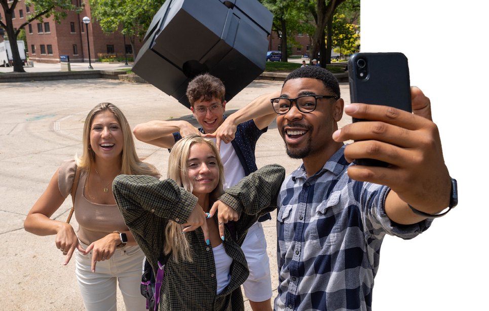 A group of students taking a selfie in front of the Cube sculpture during the summer semester.