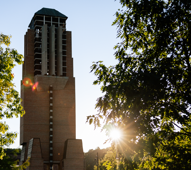 Lurie Tower and trees in the North Campus Grove are illuminated by a bright setting sun.