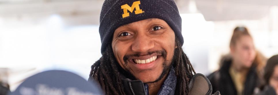 A student smiling while wearing a University of Michigan hat